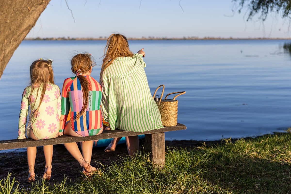 Three people sit on a bench by a calm lake in the picturesque Loddon-Mallee Region