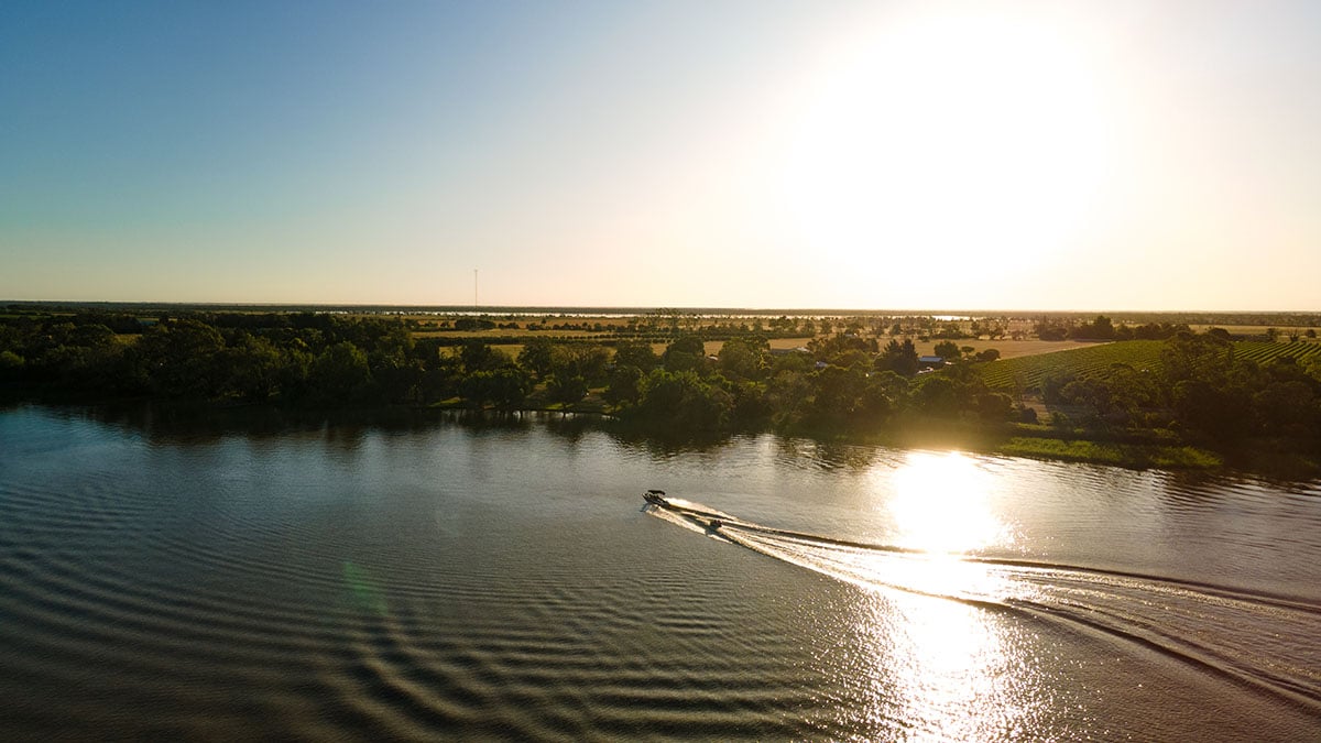 A small boat speeds across a calm river at sunset in the Loddon-Mallee Region