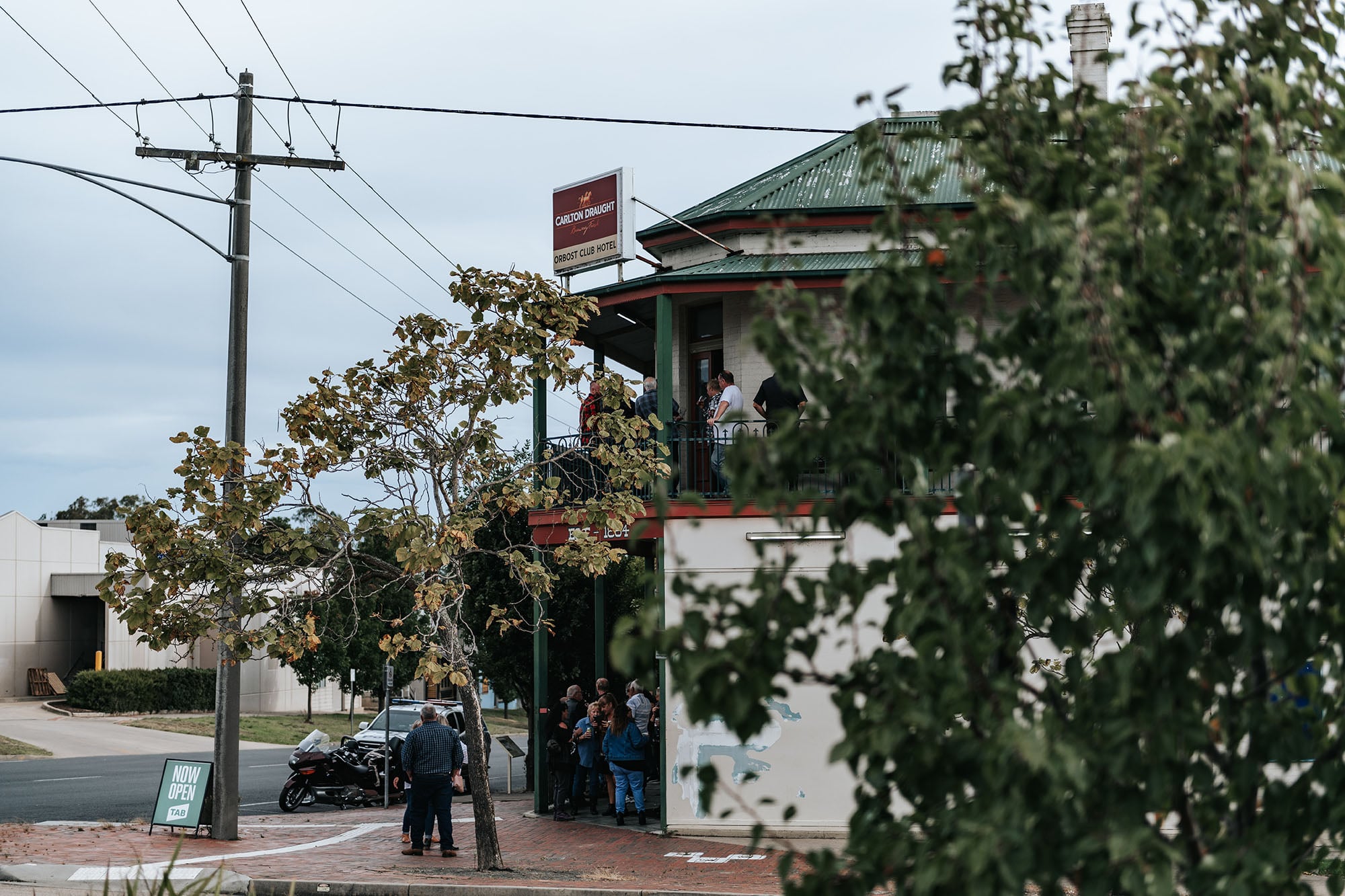 People sitting outside and on the balcony of a corner pub in Orbost